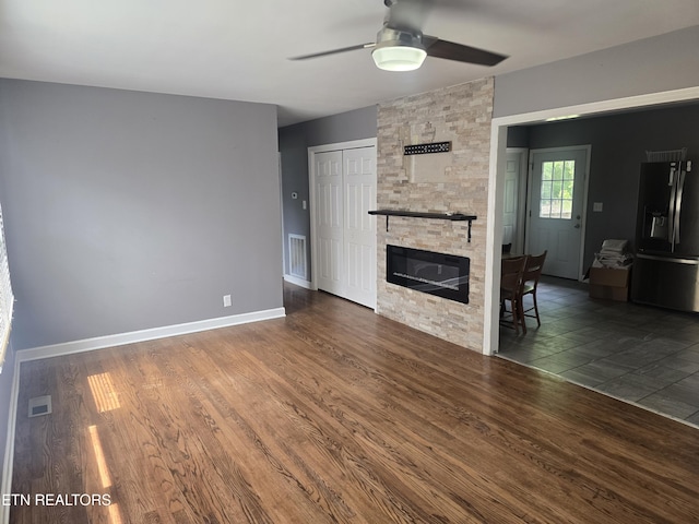 unfurnished living room with a stone fireplace, visible vents, wood finished floors, and ceiling fan