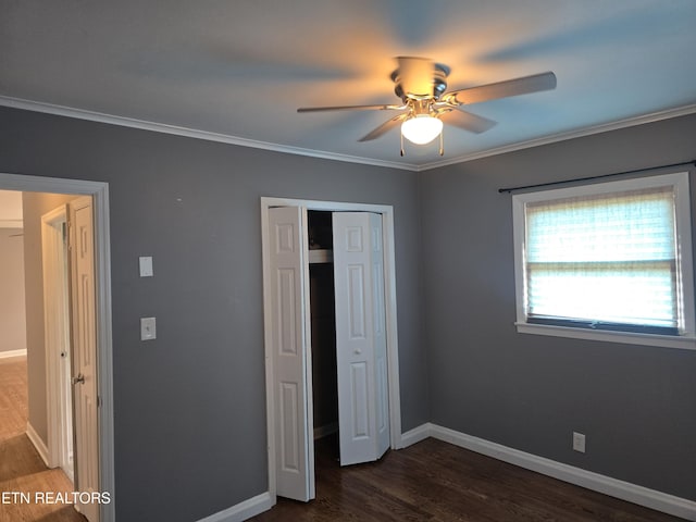 unfurnished bedroom featuring dark wood-style floors, baseboards, a closet, ceiling fan, and crown molding
