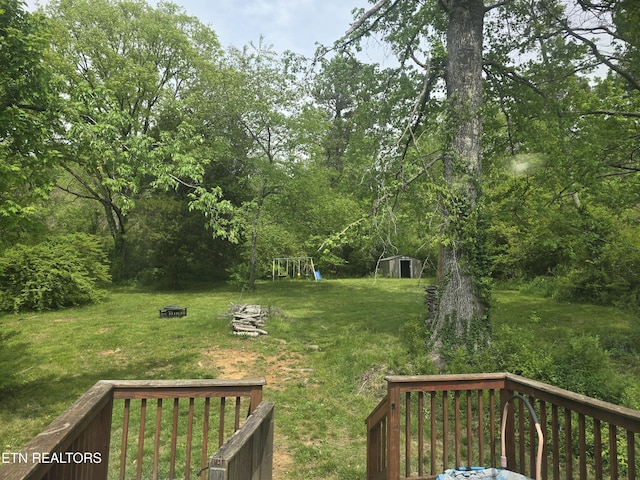 view of yard featuring an outdoor structure, a wooden deck, a playground, and a storage shed