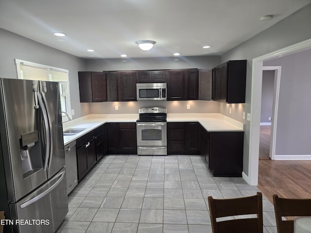 kitchen with recessed lighting, light countertops, dark brown cabinets, a sink, and appliances with stainless steel finishes