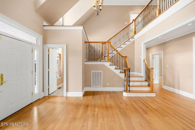 entryway with stairway, visible vents, baseboards, a towering ceiling, and wood finished floors