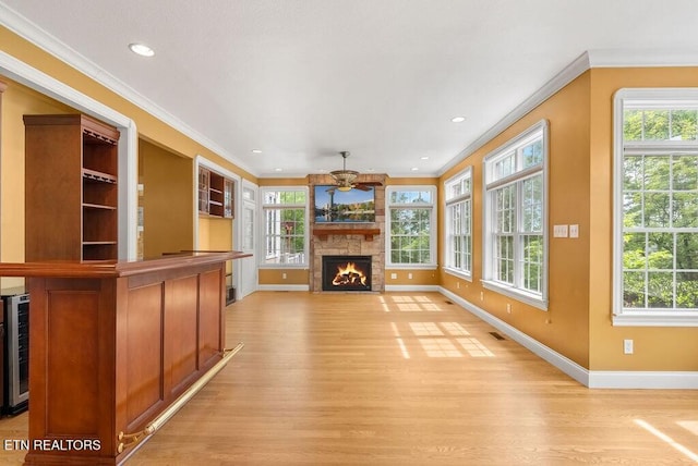 unfurnished living room featuring ceiling fan, a stone fireplace, a wealth of natural light, and light wood-type flooring