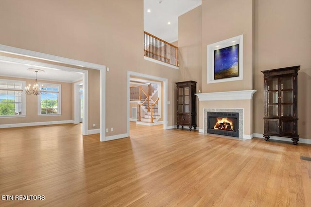 unfurnished living room with stairway, light wood-style floors, a warm lit fireplace, baseboards, and an inviting chandelier