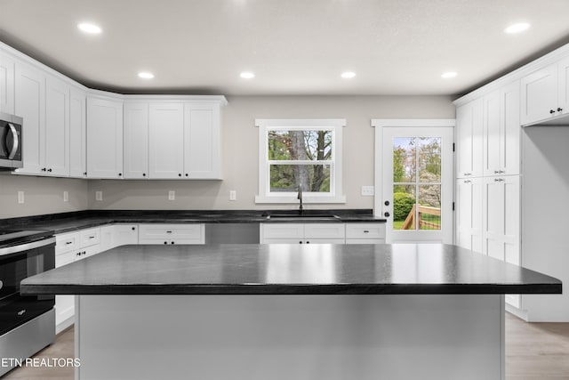 kitchen with recessed lighting, stainless steel appliances, dark countertops, a sink, and white cabinetry
