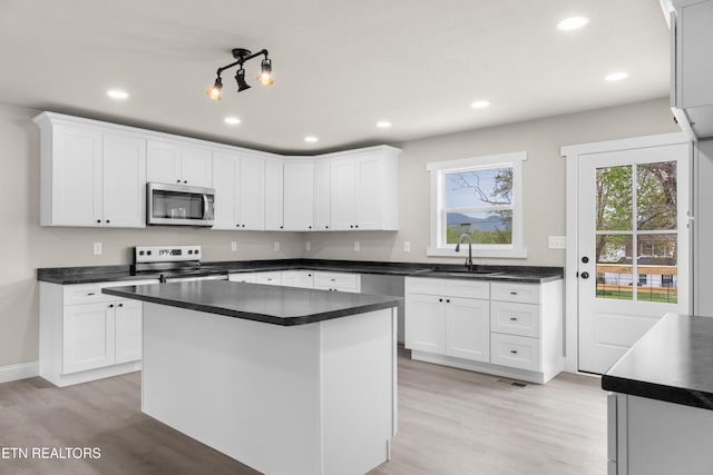 kitchen with dark countertops, stainless steel appliances, light wood finished floors, and a sink