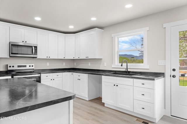 kitchen with white cabinets, recessed lighting, stainless steel appliances, dark countertops, and a sink