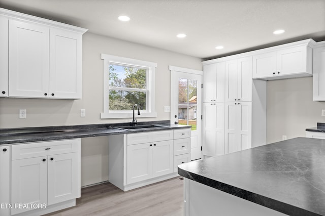 kitchen with white cabinets, dark countertops, a sink, and light wood-type flooring