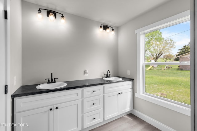 full bath featuring baseboards, wood finished floors, a sink, and double vanity