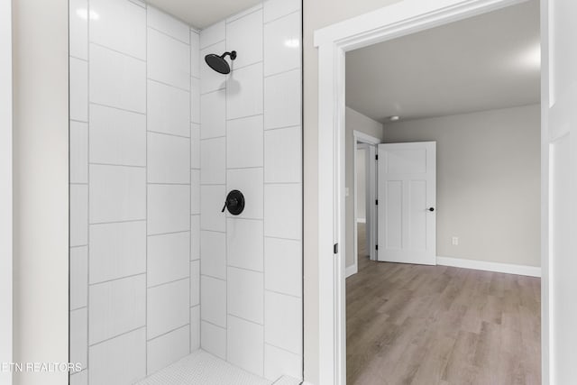 bathroom with baseboards, wood finished floors, and tiled shower