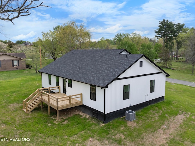 rear view of house with a lawn, a shingled roof, central AC, and a deck