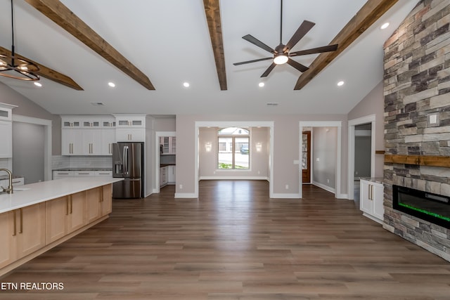 unfurnished living room with lofted ceiling with beams, baseboards, wood finished floors, ceiling fan, and a stone fireplace