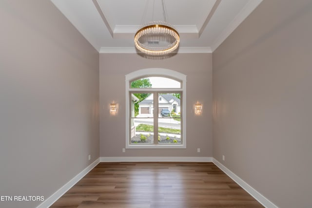 empty room featuring an inviting chandelier, ornamental molding, wood finished floors, and a raised ceiling