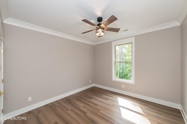 empty room featuring a ceiling fan, wood finished floors, baseboards, ornamental molding, and visible vents