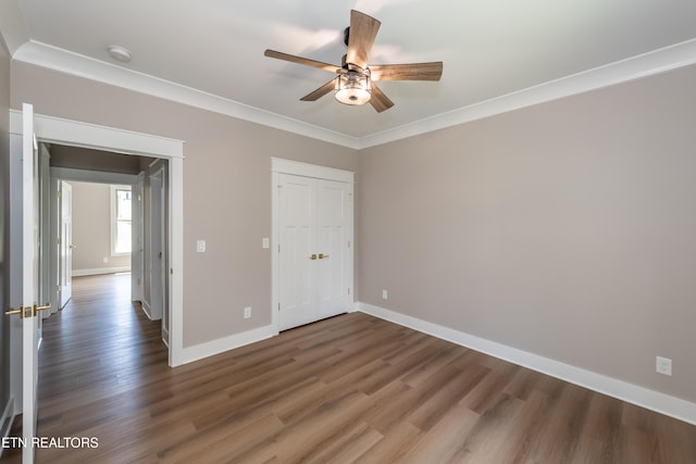 unfurnished bedroom featuring wood finished floors, a closet, crown molding, baseboards, and ceiling fan