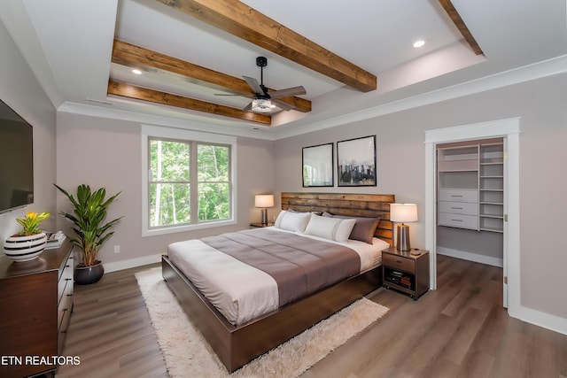 bedroom with beamed ceiling, baseboards, wood finished floors, and a spacious closet