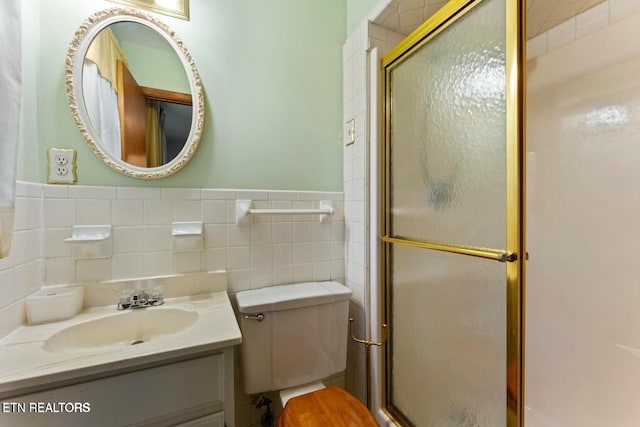 bathroom featuring a shower stall, a wainscoted wall, toilet, vanity, and tile walls