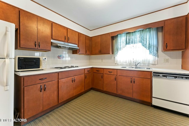 kitchen featuring under cabinet range hood, light countertops, backsplash, a sink, and white appliances