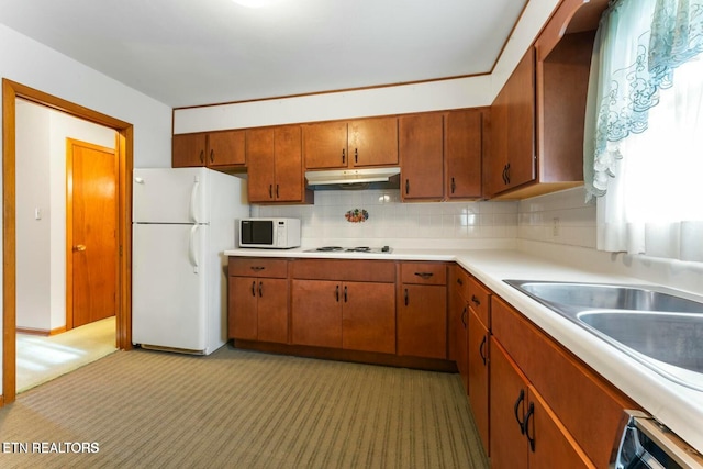 kitchen with light carpet, white appliances, brown cabinetry, light countertops, and under cabinet range hood