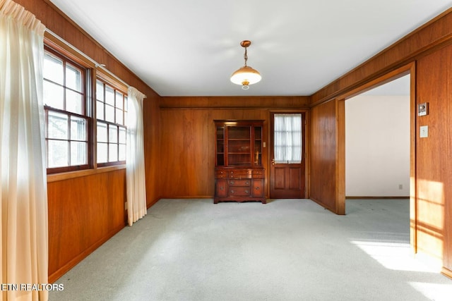 carpeted empty room featuring baseboards, wood walls, and plenty of natural light