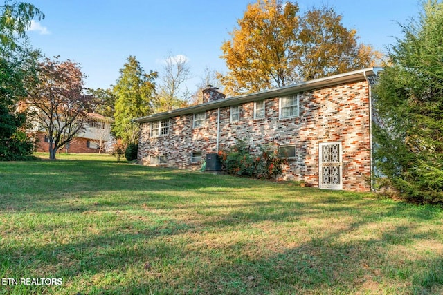back of property featuring a lawn, a chimney, brick siding, and central air condition unit