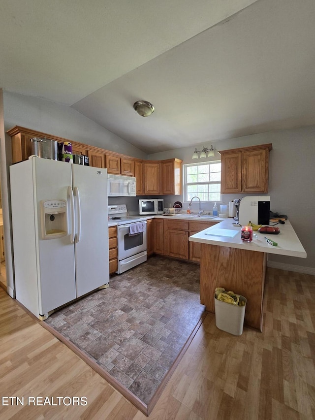 kitchen with a peninsula, a sink, white appliances, and light countertops