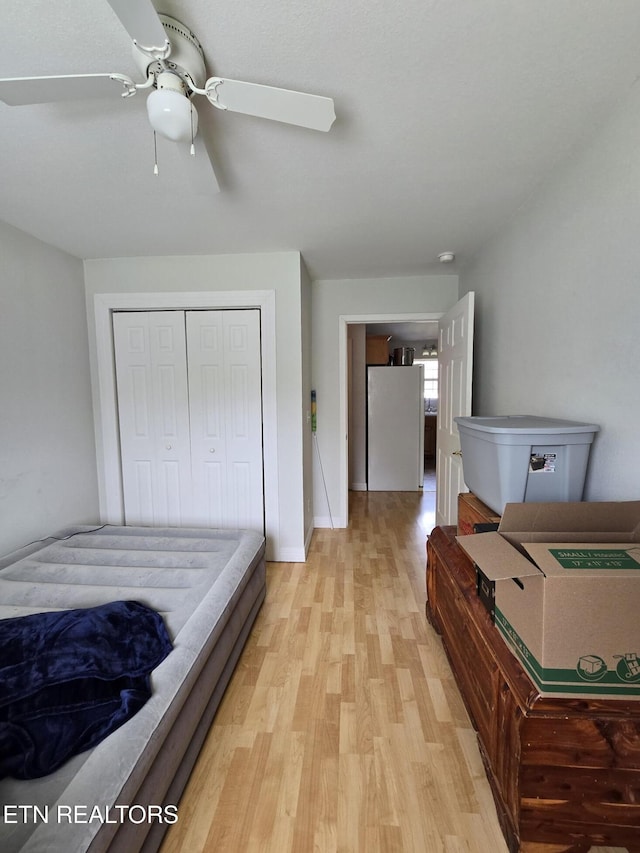 bedroom with light wood-style flooring, baseboards, freestanding refrigerator, a ceiling fan, and a closet