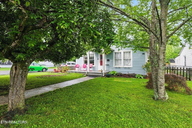 view of property hidden behind natural elements with a porch, a front yard, and fence