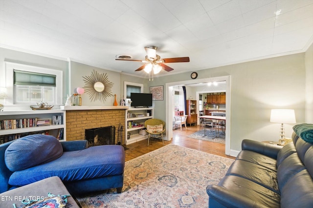 living room featuring wood finished floors, a ceiling fan, ornamental molding, and a fireplace
