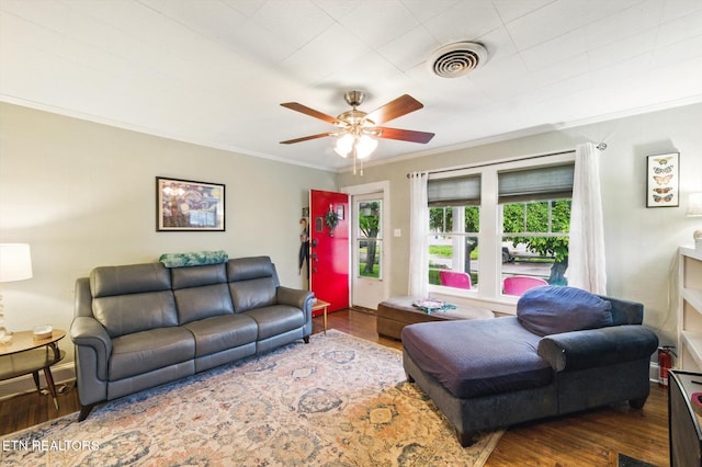living room featuring ornamental molding, a ceiling fan, visible vents, and wood finished floors