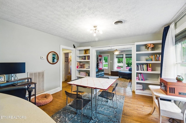dining area featuring wood finished floors, visible vents, ceiling fan, and a textured ceiling