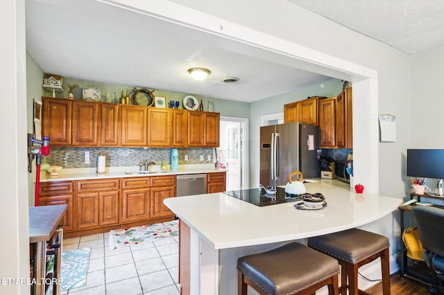 kitchen featuring appliances with stainless steel finishes, brown cabinets, a peninsula, and a sink