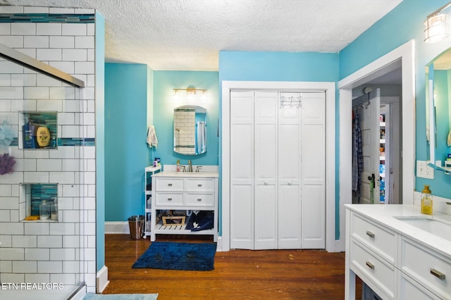 bathroom featuring a sink, a shower stall, two vanities, a textured ceiling, and wood finished floors
