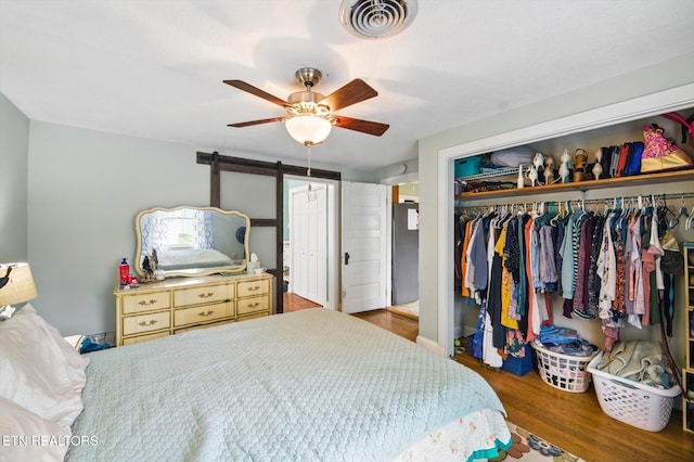 bedroom featuring a barn door, a closet, ceiling fan, visible vents, and wood finished floors