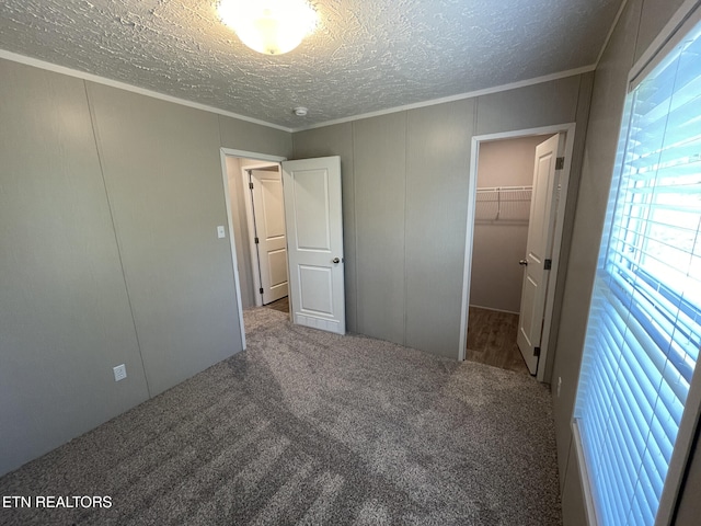 unfurnished bedroom with a walk in closet, ornamental molding, a textured ceiling, and carpet