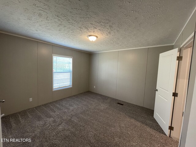 empty room with a textured ceiling, a decorative wall, carpet flooring, and ornamental molding