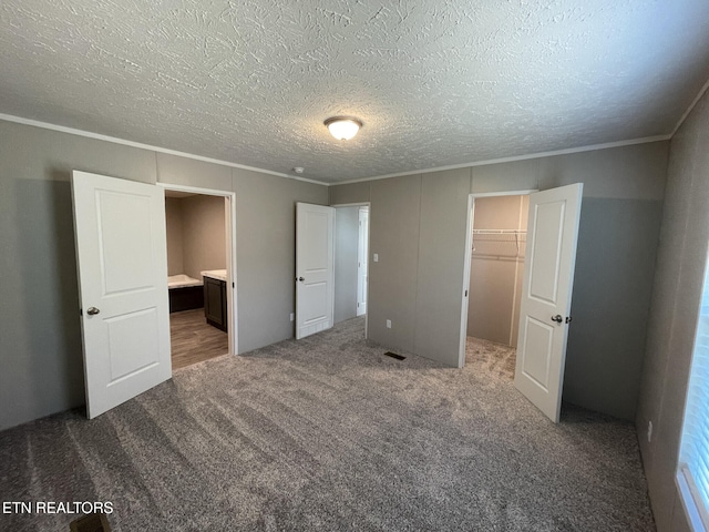 unfurnished bedroom featuring crown molding, a closet, a walk in closet, carpet flooring, and visible vents
