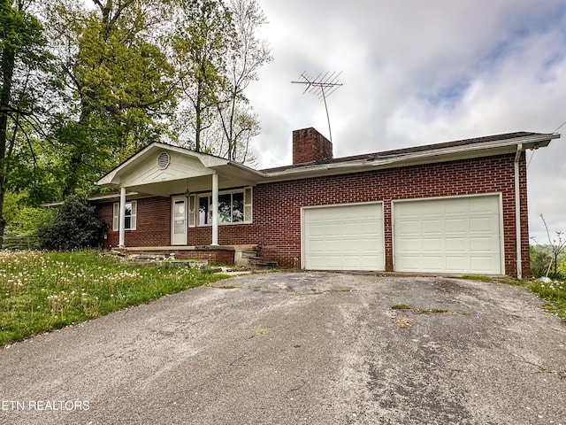 ranch-style home featuring a porch, a chimney, brick siding, a garage, and aphalt driveway