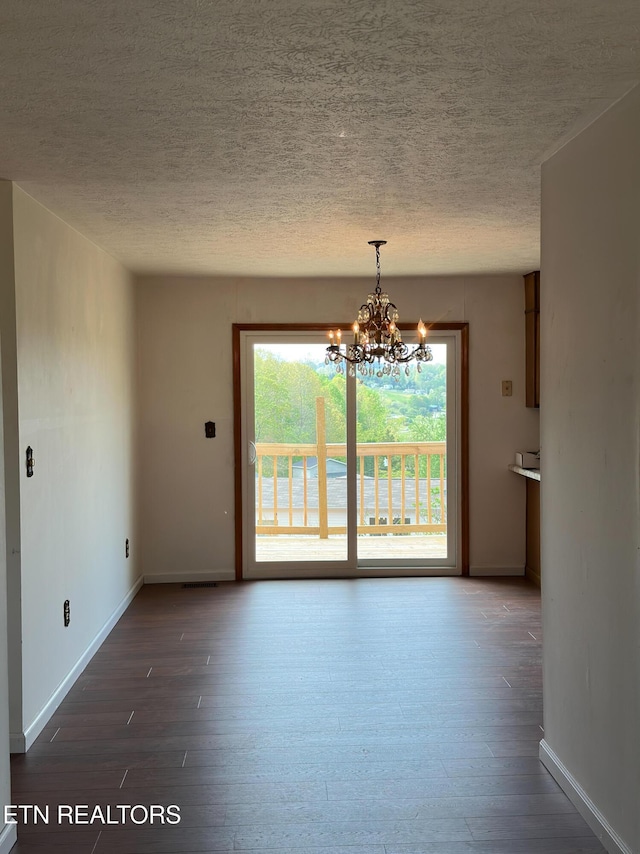 spare room featuring a chandelier, wood-type flooring, a textured ceiling, and baseboards