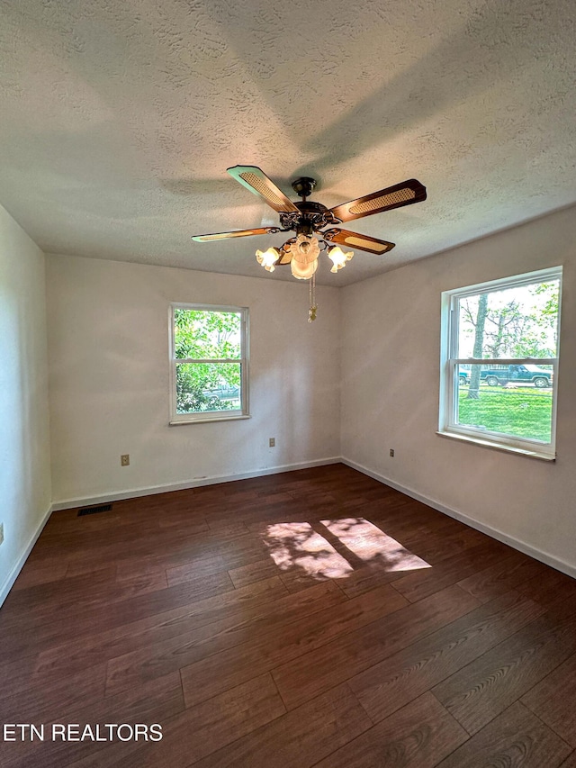 empty room with a textured ceiling, baseboards, visible vents, a ceiling fan, and hardwood / wood-style floors