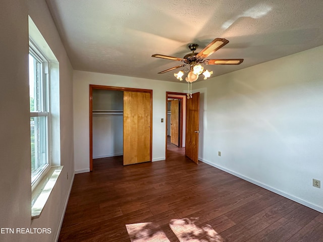 unfurnished bedroom featuring dark wood-style floors, a textured ceiling, baseboards, a closet, and ceiling fan