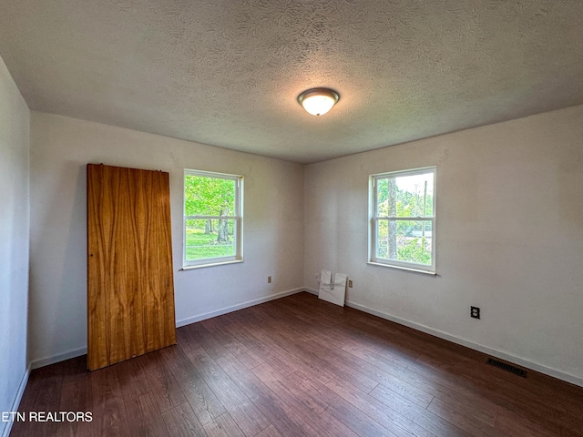 unfurnished room featuring baseboards, hardwood / wood-style floors, visible vents, and a textured ceiling