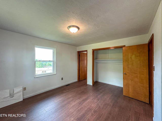 unfurnished bedroom with dark wood finished floors, a closet, baseboards, and visible vents