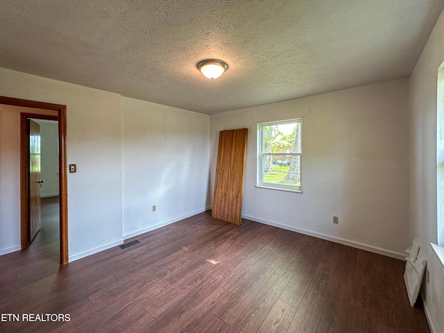 spare room featuring dark wood finished floors, baseboards, a textured ceiling, and visible vents