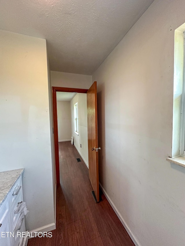 corridor with dark wood finished floors, baseboards, and a textured ceiling