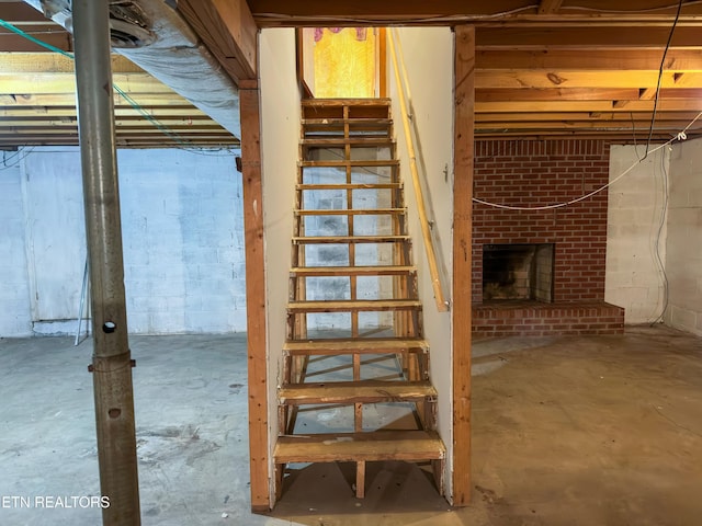 unfinished below grade area with a fireplace, concrete block wall, and stairway