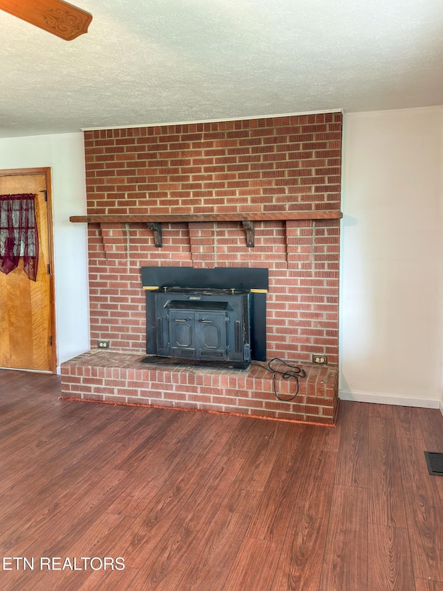 unfurnished living room with wood finished floors, a wood stove, visible vents, baseboards, and a textured ceiling