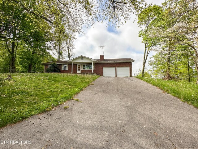 ranch-style home featuring a chimney, a front lawn, driveway, a garage, and brick siding