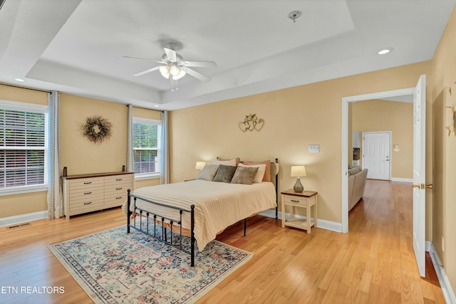 bedroom with a raised ceiling, baseboards, light wood finished floors, and visible vents