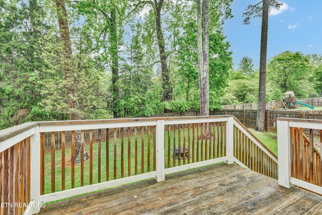 wooden deck featuring a fenced backyard, a playground, and a lawn