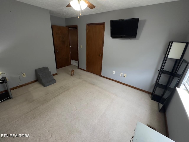 unfurnished bedroom featuring light colored carpet, baseboards, a ceiling fan, and a textured ceiling